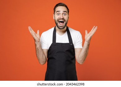 Young Surprised Fun Man 20s Barista Bartender Barman Employee In Black Apron White T-shirt Work In Coffee Shop Spread Hands Isolated On Orange Background Studio Portrait Small Business Startup Concept