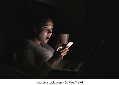 Young Surprised Girl Sitting In Bed In The Evening And Watching A Scary Movie On Her Laptop