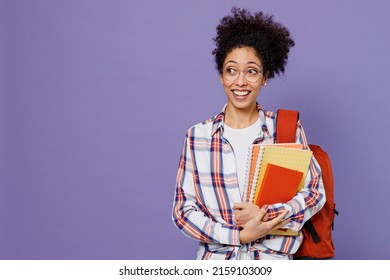 Young surprised girl woman of African American ethnicity teen student in shirt backpack hold books look aside isolated on plain purple background. Education in high school university college concept