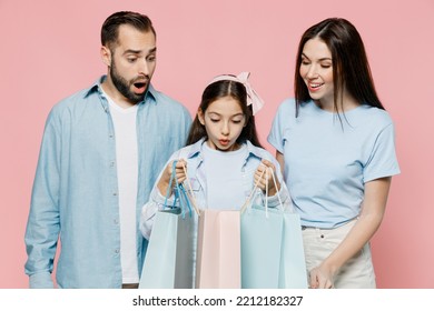 Young Surprised Happy Fun Parents Mom Dad With Child Kid Daughter Teen Girl In Blue Clothes Holding Package With Purchases After Shopping Look At Bags Isolated On Plain Pastel Light Pink Background.