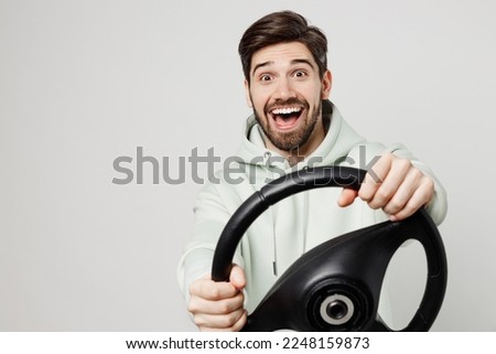 Young surprised happy fun satisfied amazed caucasian man wear mint hoody look camera hold steering wheel driving car isolated on plain solid white background studio portrait. People lifestyle concept