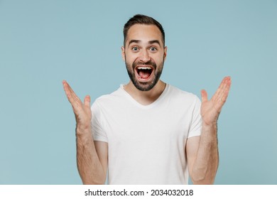 Young Surprised Happy Impressed Man In Blank Print Design Casual White T-shirt Look Camera Spread Hands Isolated On Plain Pastel Light Blue Color Background Studio Portrait. People Lifestyle Concept