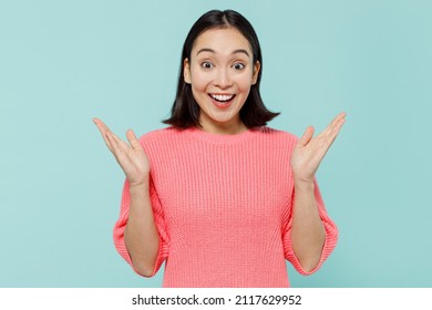 Young surprised happy woman of Asian ethnicity 20s wearing pink sweater spread hands say wow cool awesome isolated on pastel plain light blue color background studio portrait. People lifestyle concept