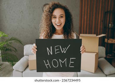 Young surprised happy woman wear casual clothes sits near grey sofa couch hold card sign with new home title text stay at flat rest relax spend free spare time in living room indoor. Lounge concept - Shutterstock ID 2367234495