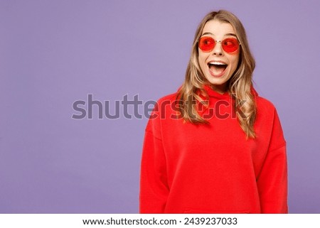 Young surprised shocked fun blonde woman she wears red hoody casual clothes sunglasses look aside on area mock up isolated on plain pastel light purple background studio portrait. Lifestyle concept