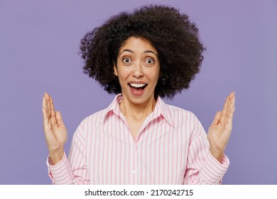 Young surprised shocked impressed amazed woman of African American ethnicity 20s wear pink white striped shirt spread hnads look camera isolated on plain pastel light purple background studio portrait