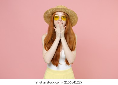 Young surprised shocked redhead woman 20s ginger long hair wear straw hat glasses summer clothes covering mouth with hands looking camera keep secret isolated on pastel pink background studio portrait