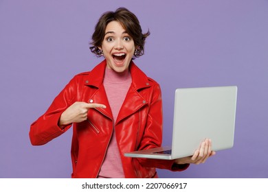 Young Surprised Shocked Woman 20s Wear Red Leather Jacket Hold Use Work Point Finger On Laptop Pc Computer Isolated On Plain Pastel Light Purple Background Studio Portrait. People Lifestyle Concept