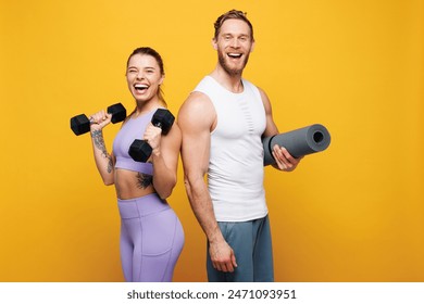 Young surprised strong fitness trainer instructor sporty two man woman wear blue clothes spend time in home gym hold yoga mat dumbbells isolated on plain yellow background. Workout sport fit concept - Powered by Shutterstock