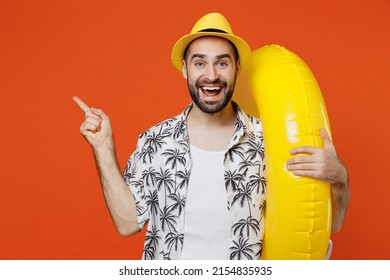 Young surprised tourist man in beach shirt hat hold inflatable ring point index finger aside on workspace isolated on plain orange background studio portrait. Summer vacation sea rest sun tan concept