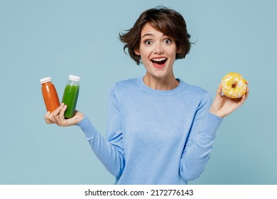 Young surprised woman in casual sweater hold pressed juice green orange vegetable smoothie as detox diet put arm on belly isolated on plain pastel light blue background. People lifestyle food concept - Shutterstock ID 2172776143