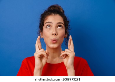 Young Surprised Woman Holding Fingers Crossed For Good Luck Isolated Over Blue Background