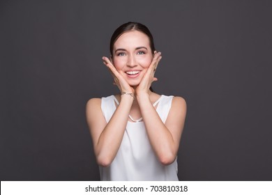 Young surprised woman holding her head portrait. Beautiful girl heard good news, posing at camera, dark background