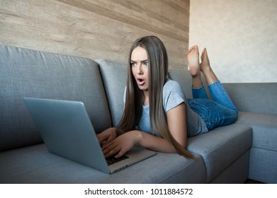 Young surprised woman lying relaxed on belly on sofa with  laptop 
