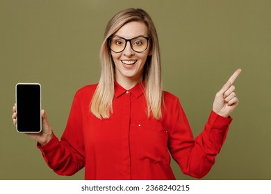 Young surprised woman she wearing red shirt casual clothes glasses hold in hand use mobile cell phone with blank screen workspace area pont index finger aside isolated on plain pastel green background - Powered by Shutterstock