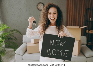 Young surprised woman wear casual clothes sits near grey sofa couch hold card sign with new home title text, keys stay at flat rest relax spend free spare time in living room indoor. Lounge concept - Shutterstock ID 2365041241