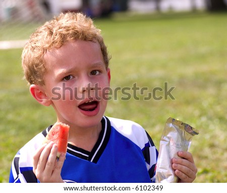 Young sweaty boy having halftime snack of watermelon and juice