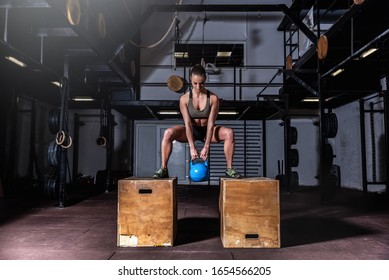 Young sweaty muscular fit girl with big muscles and strong legs doing deep squat and dip on two wooden jump boxes with heavy kettlebell for hardcore cross strength workout training in the gym  - Powered by Shutterstock