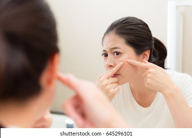 Young Sweet Woman Looking At Bathroom Mirror Reflection Image And Hands Touch Cheek Squeeze Acne When Maintaining Face Care Finding Unhealthy Problem.