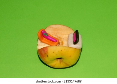 A Young Sweet Worm Watches A Movie At Home In His Apple While Lying On An Orange Bed On A Green Background