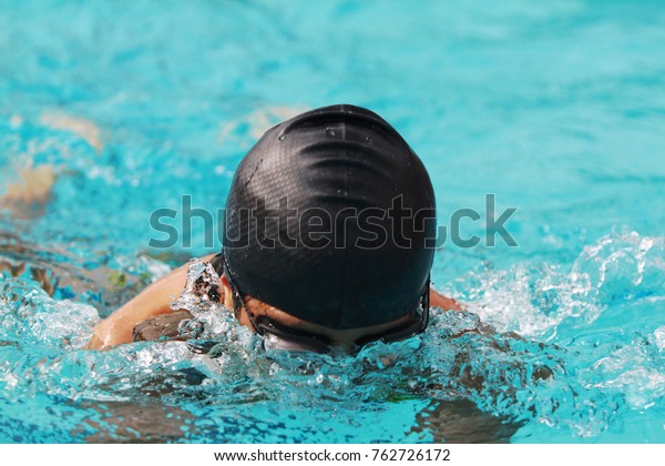 Young swimmer with black\
swimming cap swims breast stroke in the swimming pool for\
competition, close up