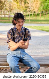 Young Taiwanese Man Smiling And Using The Smartphone Sitting A Bench At Street.