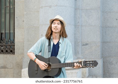 Young talented street musician passionately plays the guitar and sings soulful melodies, captivating passersby with his music on a lively and colorful street.