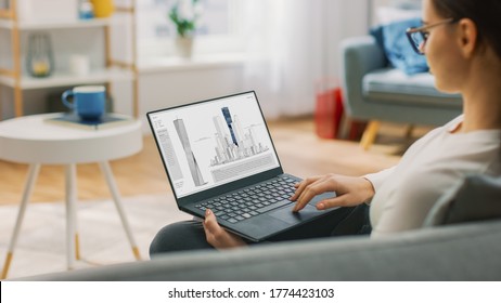 Young Talented Woman Architect is Sitting at Home on a Couch Working with a Laptop Computer under Futuristic Concept 3D Model of Modern Skyscraper. - Shutterstock ID 1774423103