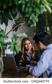 A young, tanned and attractive Southeast Asian woman in a suit is interviewing for a job to advance her career. She is smiling as she talks to her interviewer, a Chinese manager in a coworking office.