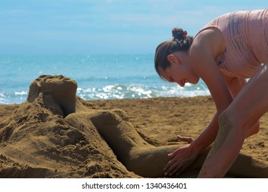 Young tanned girl in a bathing suit close-up on the beach sculpts sand sculpture of sand, a girl lying on the beach in summer sunny day - Powered by Shutterstock