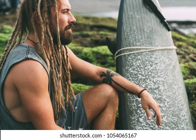 Young tanned surfer with long dreadlocks and beautiful tattoos sitting and watching the ocean on the mossy rocks in Indonesia, Bali, Canggu, Batu Bolong Beach. - Powered by Shutterstock