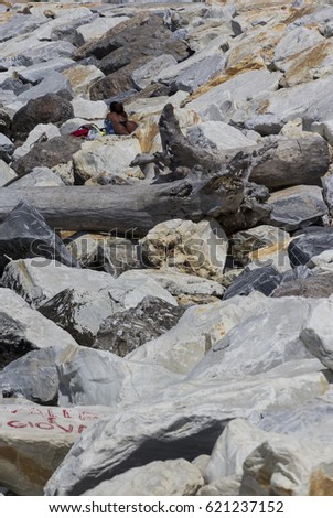 Young tanned woman in bikini thong is sunbathing ensconced amidst rocks