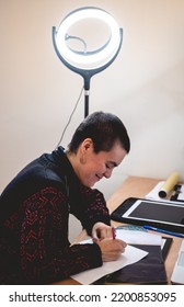 Young Tattoo Artist Girl With Very Short Hair Making The Design Of A Tattoo Of Yin Yang On A Desk With A Led Ring Light