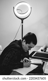 Young Tattoo Artist Girl With Very Short Hair Making The Design Of A Tattoo Of Yin Yang On A Desk With A Led Ring Light (in Black And White)