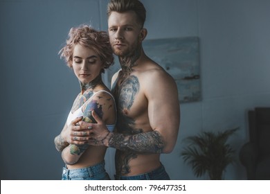 Young Tattooed Couple Hugging In Bedroom