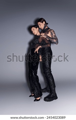 A young tattooed couple posing gracefully in a studio against a grey background.