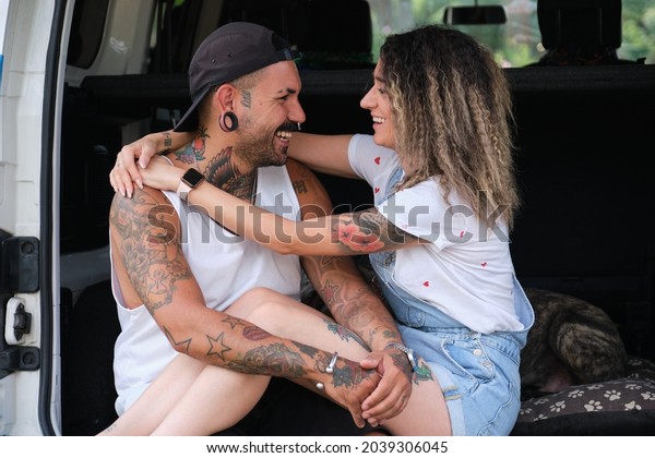 Young tattooed couple smile, hug and look each other\
in the back of the van.