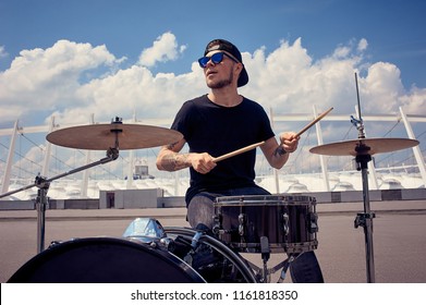 young tattooed drummer in sunglasses playing drums on street