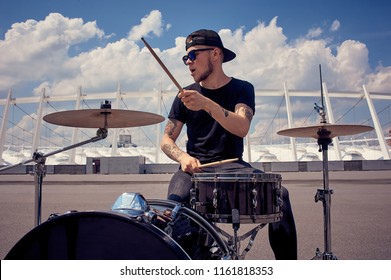 young tattooed drummer in sunglasses playing drums on street