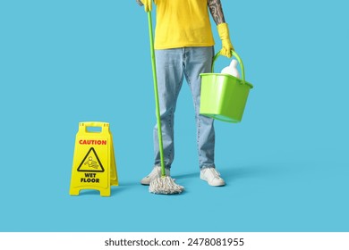 Young tattooed man with cleaning supplies and caution sign on blue background - Powered by Shutterstock