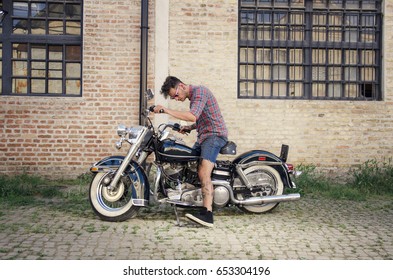 Young Tattooed Man Sitting On A Vintage Motorcycle ,  Side View , Grungy Brick Wall Background 