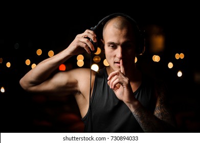 Young and tattooed nightclub DJ in headphones feels the music on the background of night club lights - Shutterstock ID 730894033