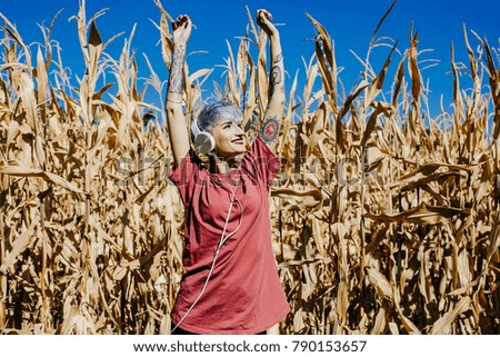 
Young tattooed woman dancing while listening to music with her headphones. Dance free and happy in front of a wheat field on a sunny day. Lifestyle