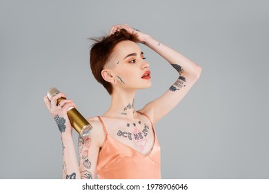 Young Tattooed Woman With Red Lips Using Hairspray Isolated On Grey