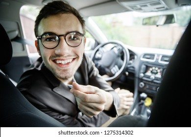 Young taxi driver showing "money" sign while looking at the camera. He is sitting at his car.