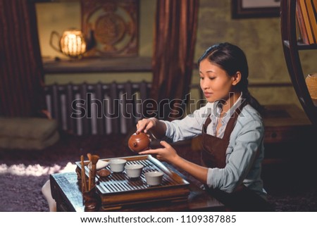 Young tea master pouring tea in room