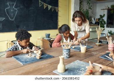 Young Teacher In Apron Sculting With Kids And Assisting Them At Ceramics Class