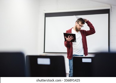 Young Teacher With Beard In Brown Hoodie Thinking In Empty Classroom Near The Whiteboard