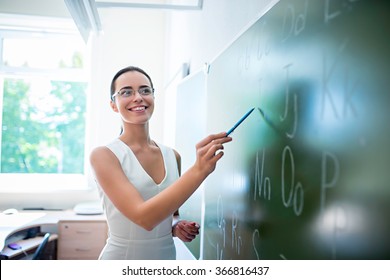 Young Teacher At Blackboard In Classroom