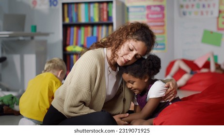 Young teacher cheering and calming upset African-American girl in kindergarten. Female teacher hug and comfort sad kid in nursery school - Powered by Shutterstock